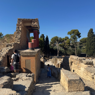 The reconstructed ruins of Knossos Palace, with visitors walking through the ancient stone corridors.