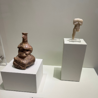 A small clay figurine of a squatting woman from Neolithic Crete, displayed beside a later marble figure.