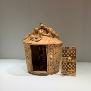 A circular clay shrine model with figures looking in through the roof.